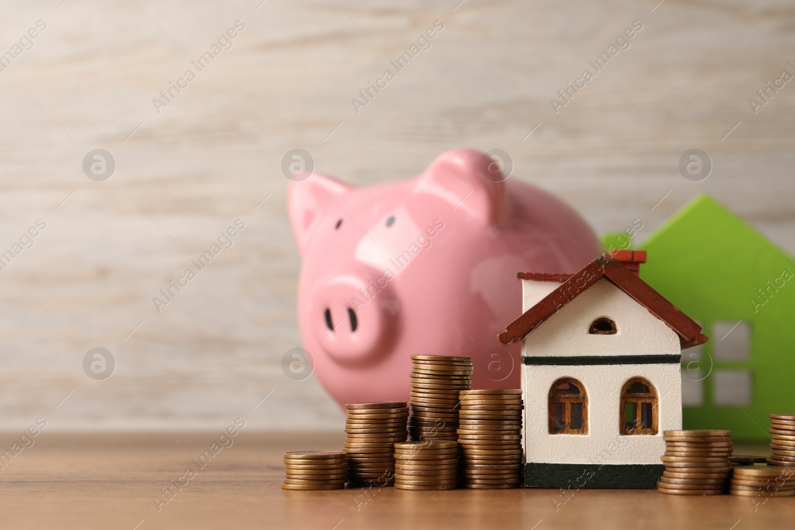 Photo of House models, piggy bank and stacked coins on wooden table, selective focus. Space for text