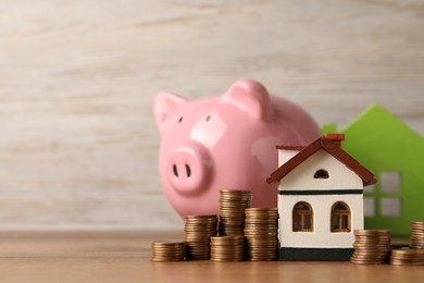 Photo of House models, piggy bank and stacked coins on wooden table, selective focus. Space for text