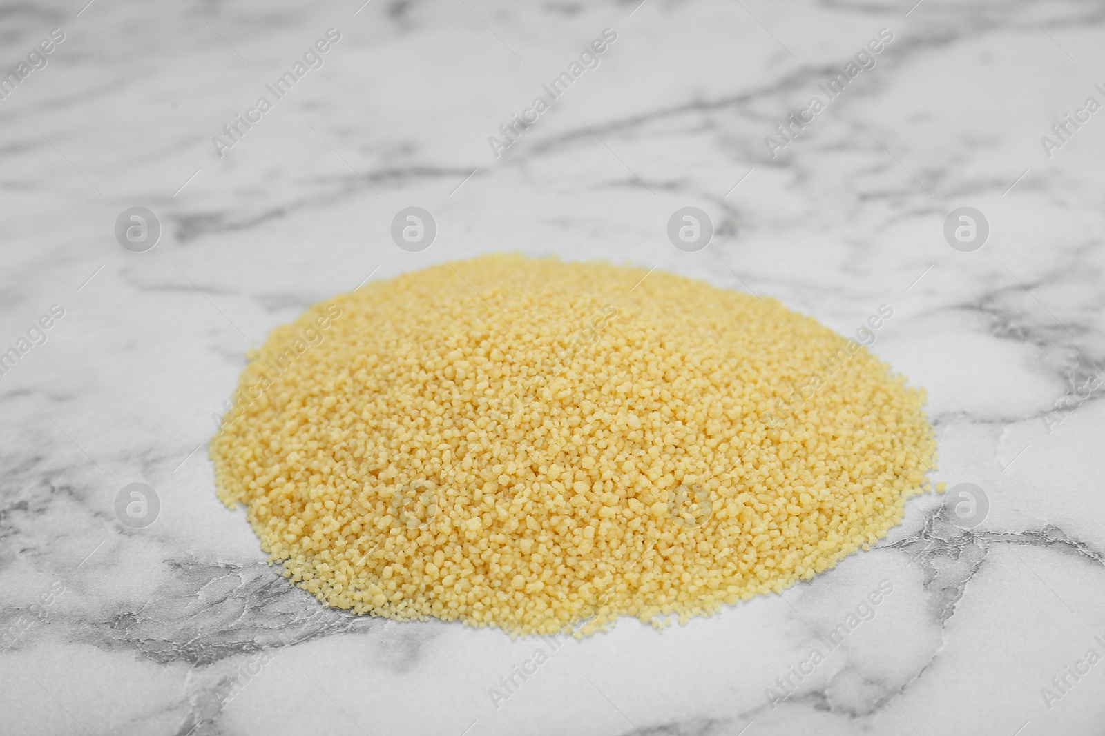 Photo of Heap of raw couscous on white marble table