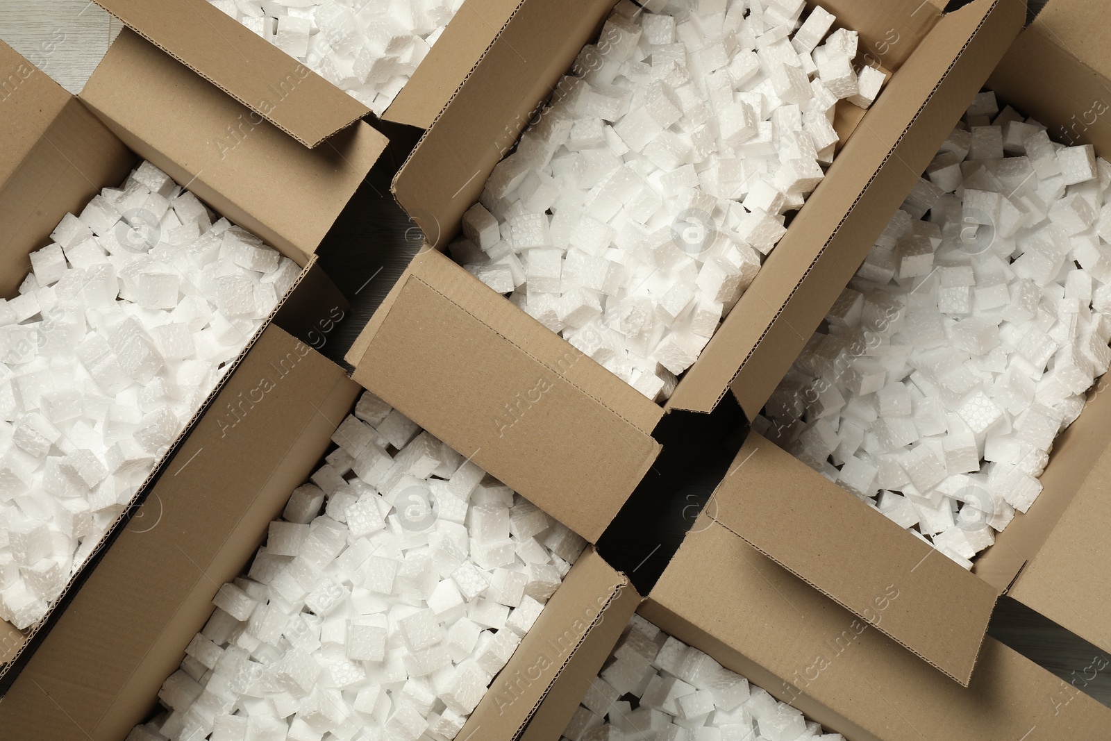 Photo of Open cardboard boxes with pieces of polystyrene foam on floor, flat lay. Packaging goods