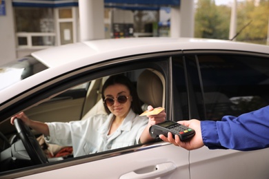 Photo of Woman sitting in car and paying with credit card at gas station, focus on hand