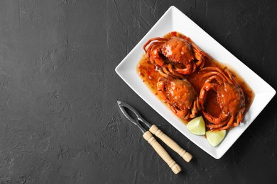 Photo of Delicious boiled crabs with sauce and lime served on black textured table, top view. Space for text