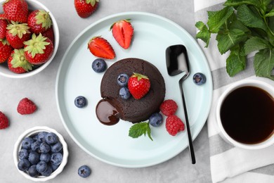Photo of Plate with delicious chocolate fondant, berries and mint on grey table, flat lay