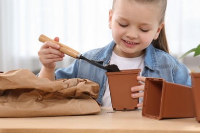 Photo of Cute little girl planting seedling into pot at wooden table indoors