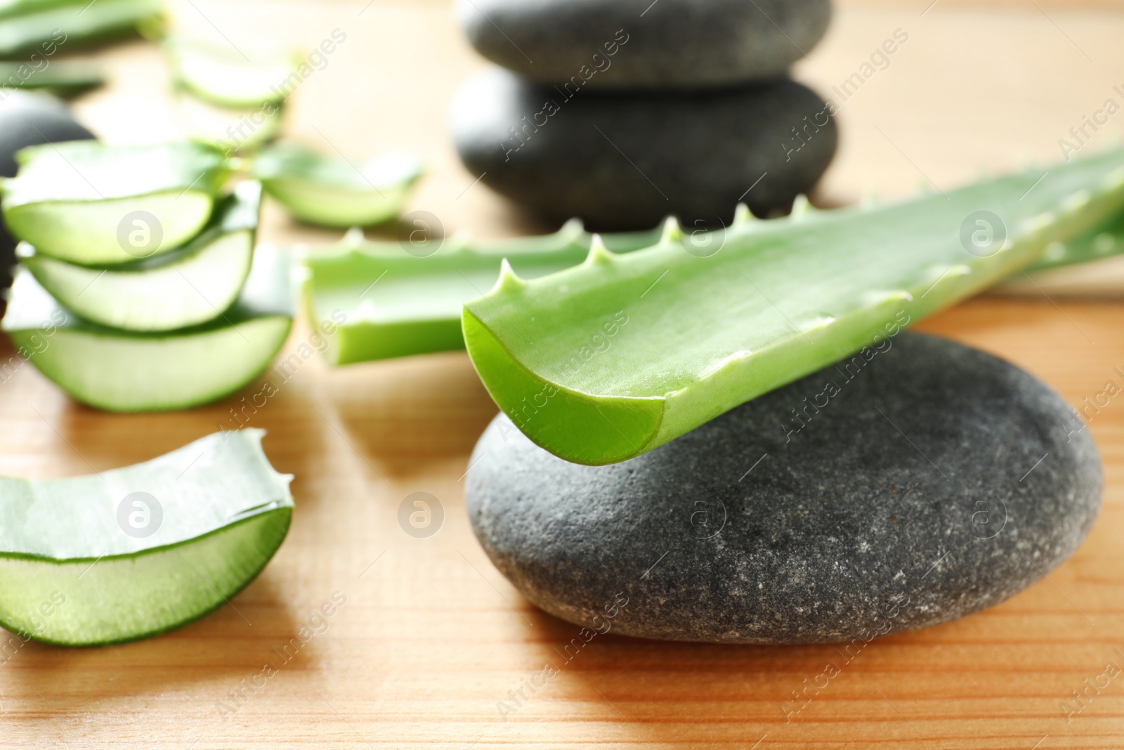 Photo of Fresh aloe vera leaves and spa stones on wooden table, closeup