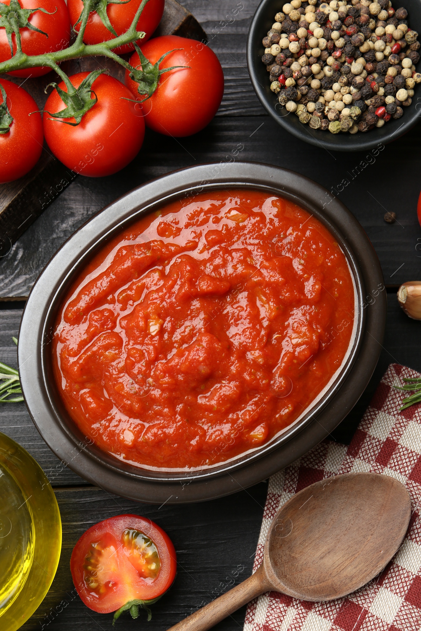 Photo of Homemade tomato sauce in bowl, spoon and fresh ingredients on black wooden table, flat lay