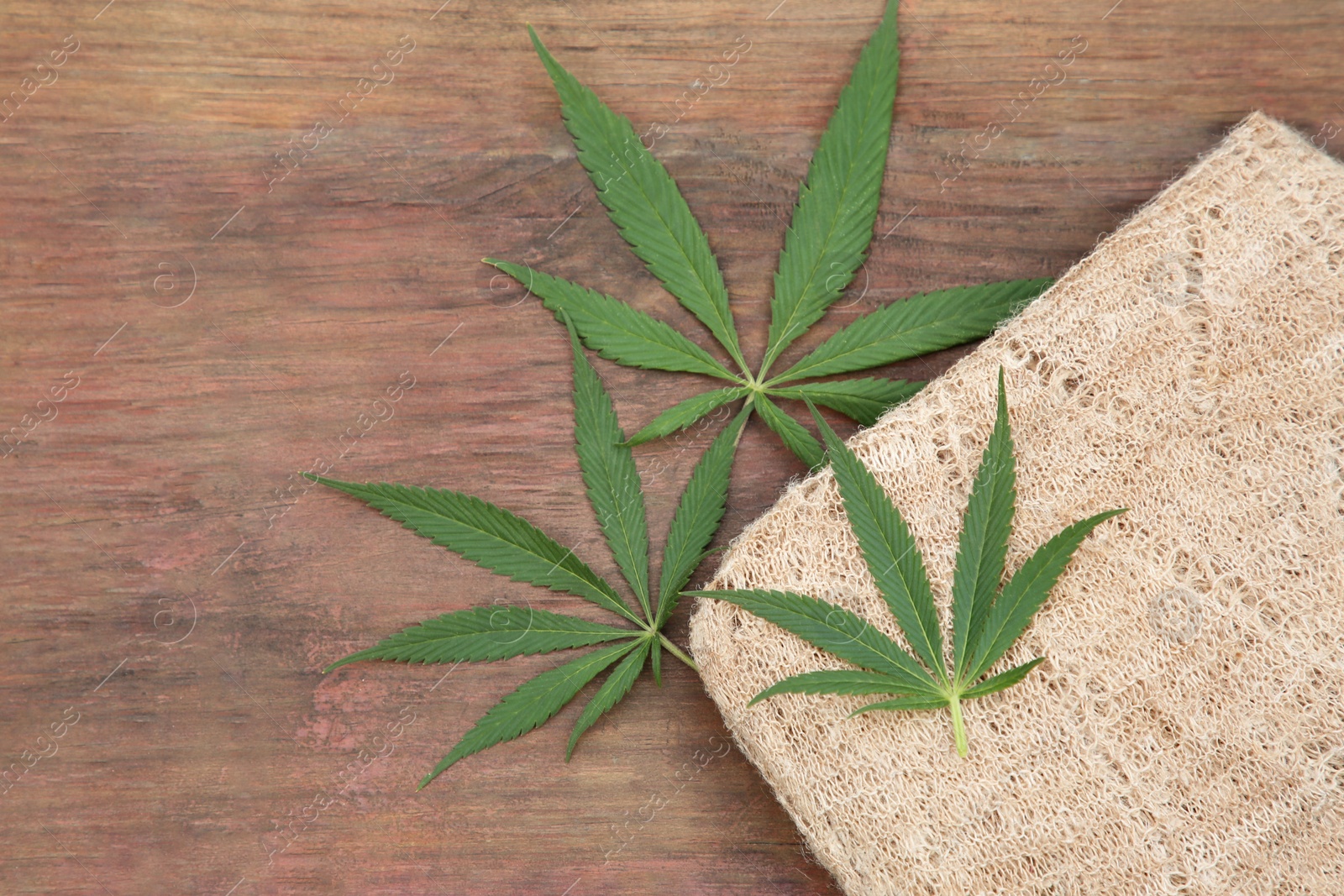 Photo of Hemp cloth and green leaves on wooden table, flat lay. Space for text