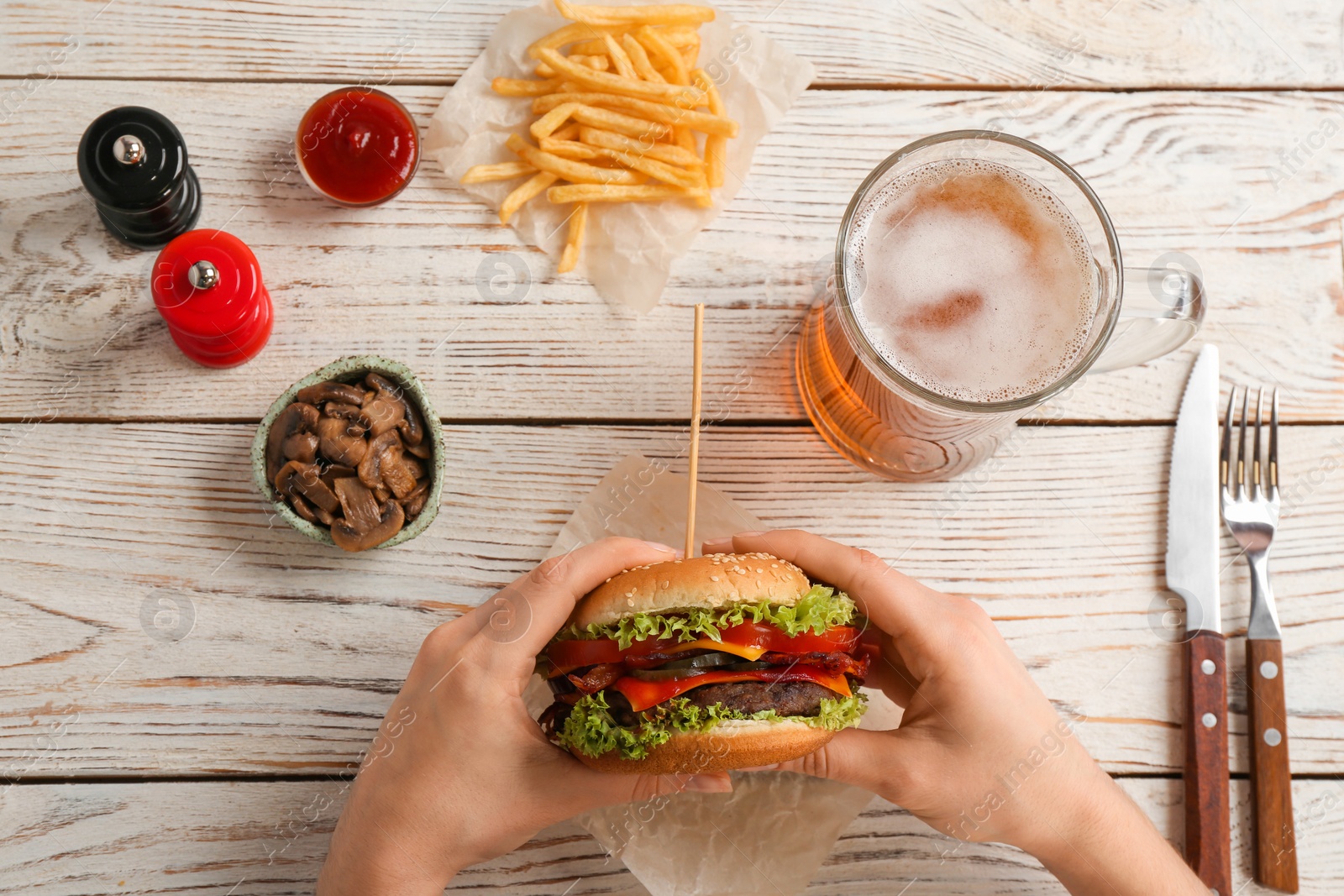 Photo of Woman holding tasty burger with bacon over wooden table, top view