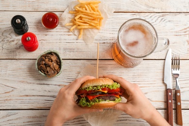 Photo of Woman holding tasty burger with bacon over wooden table, top view