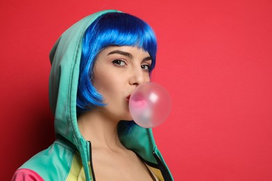 Photo of Fashionable young woman in colorful wig blowing bubblegum on red background, space for text