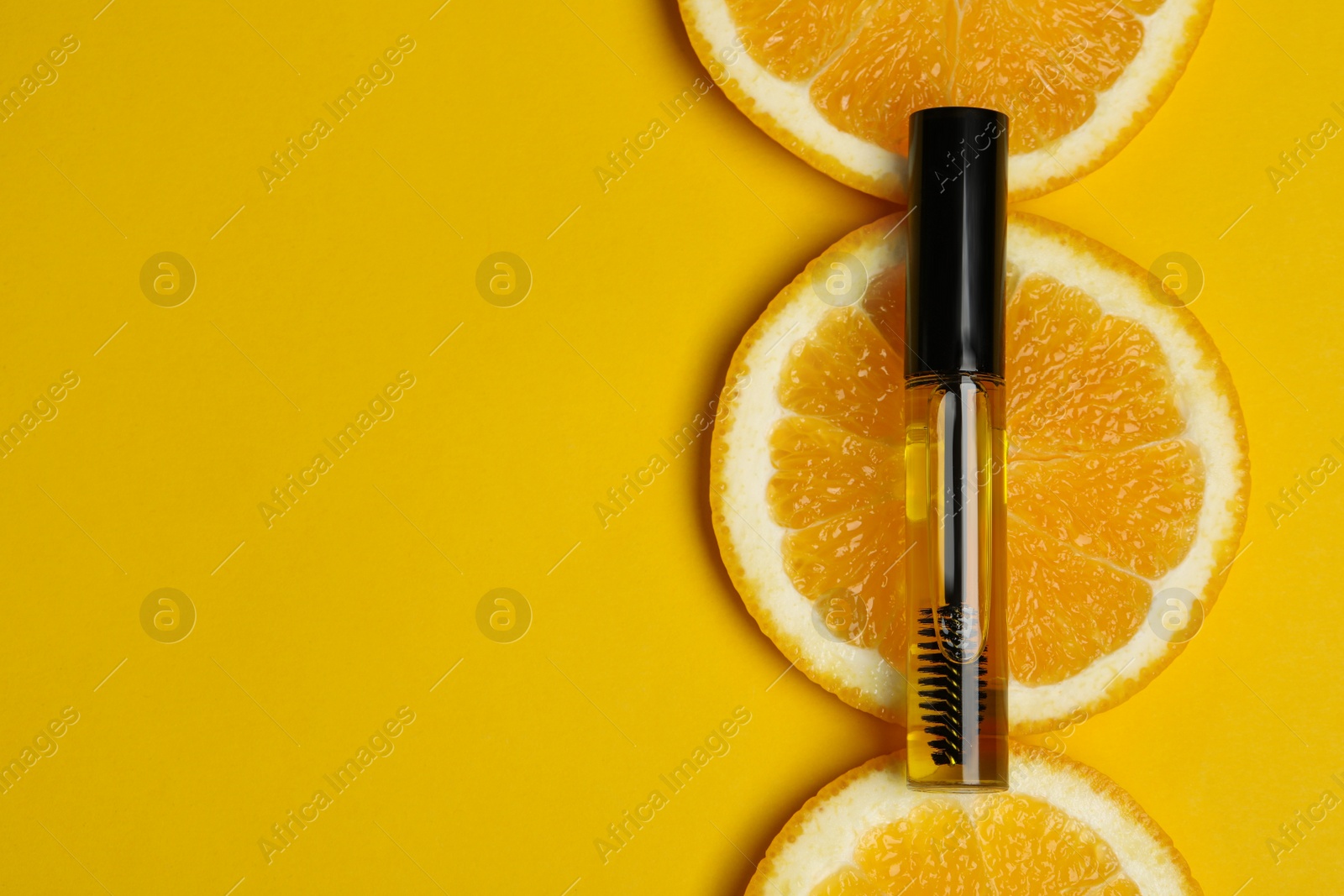 Photo of Tube of eyelash oil with fresh orange slices on yellow background, flat lay. Space for text