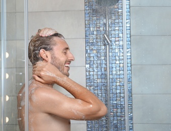 Photo of Attractive young man taking shower with soap in bathroom. Space for text