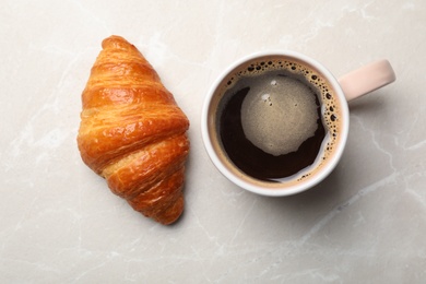 Cup of coffee and croissant on light background, flat lay