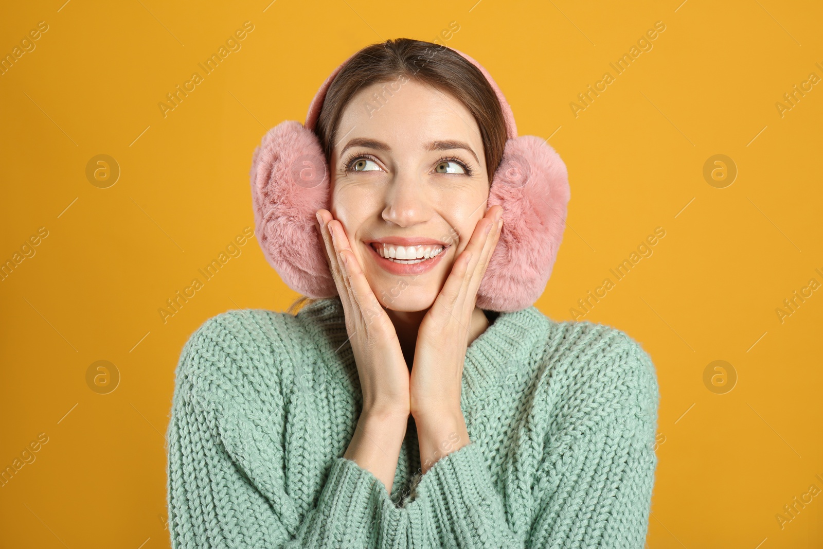 Photo of Happy woman wearing warm earmuffs on yellow background