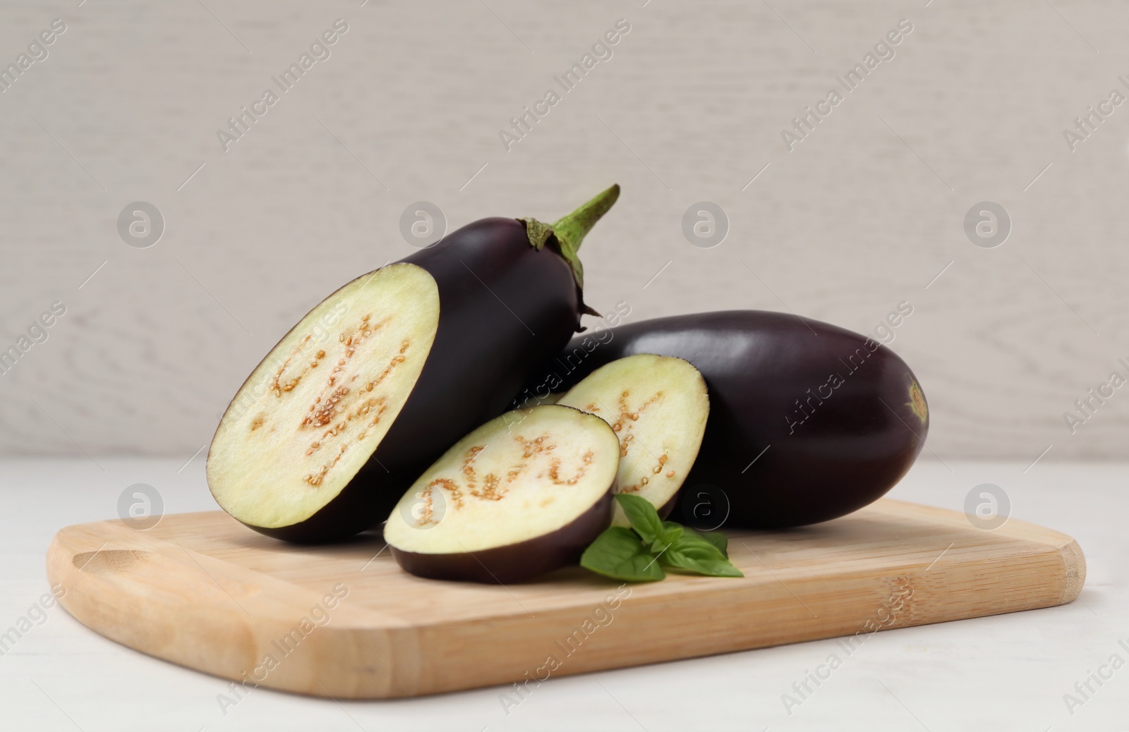 Photo of Cut and whole purple eggplants with basil on white table