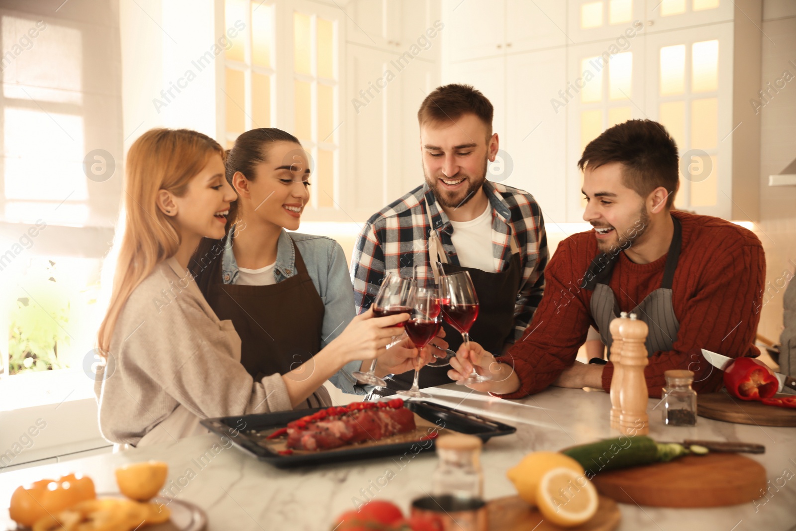 Photo of Happy people drinking wine while cooking food in kitchen