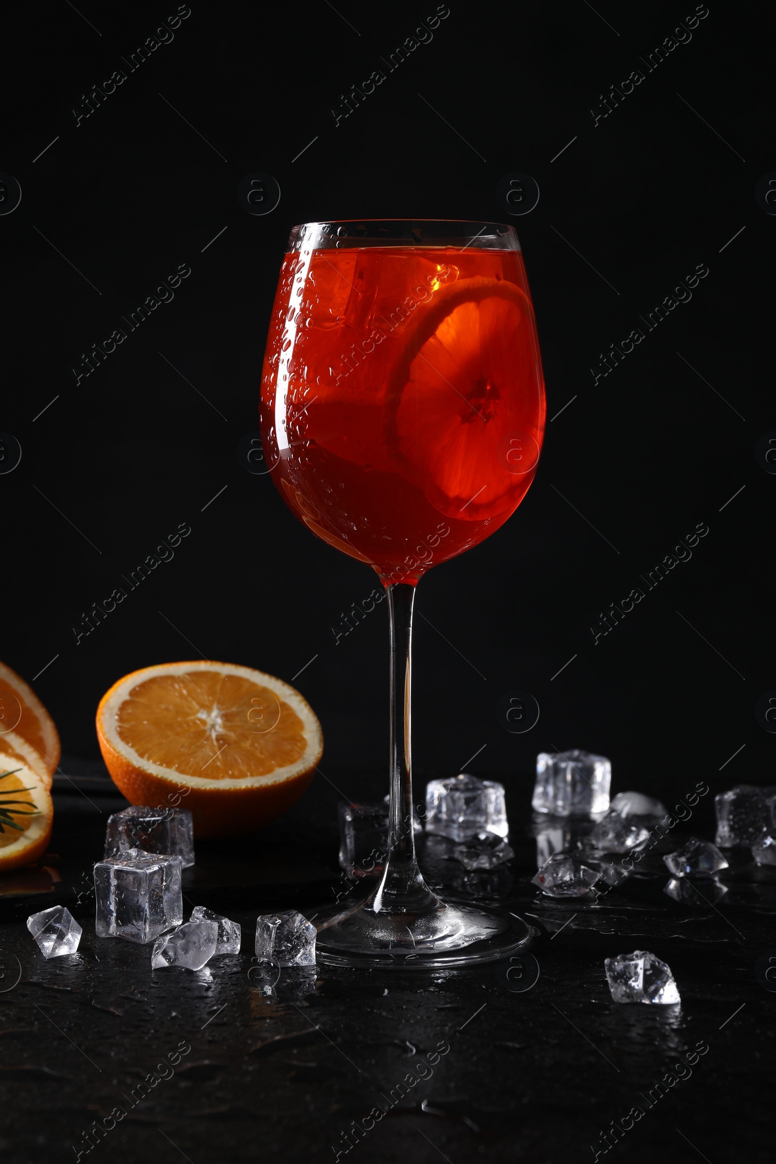 Photo of Glass of tasty Aperol spritz cocktail with orange slices and ice cubes on table against black background