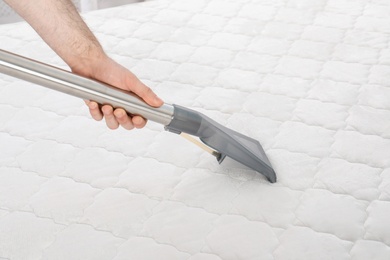 Man disinfecting mattress with vacuum cleaner, closeup. Space for text