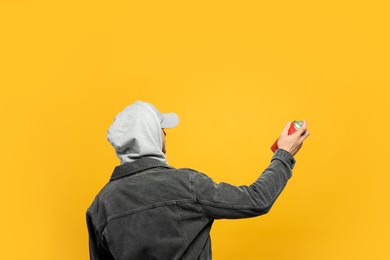 Photo of Man holding can of spray paint on yellow background, back view