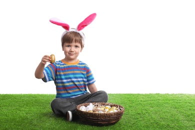 Cute little boy wearing bunny ears with basket full of dyed Easter eggs on green grass