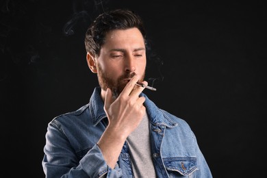 Man using cigarette holder for smoking on black background, space for text