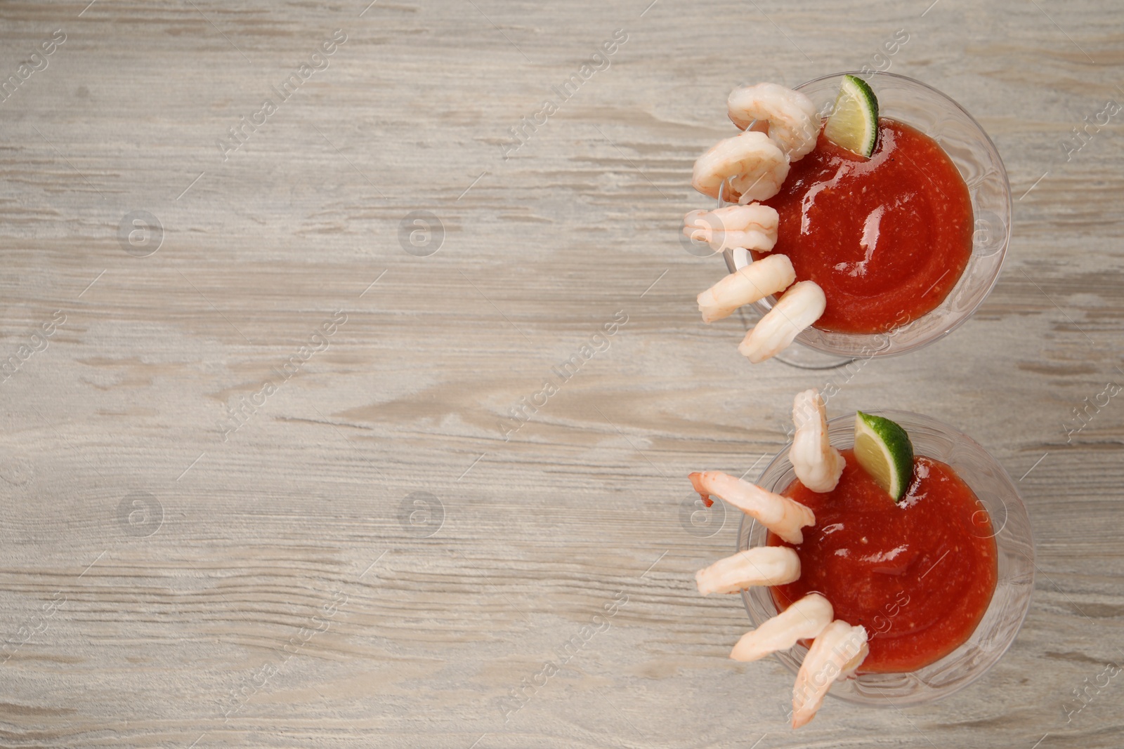 Photo of Tasty shrimp cocktail with sauce and lime in glasses on wooden table, flat lay. Space for text