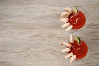 Photo of Tasty shrimp cocktail with sauce and lime in glasses on wooden table, flat lay. Space for text