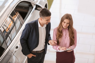 Photo of Young saleswoman working with client in car dealership