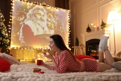 MYKOLAIV, UKRAINE - DECEMBER 24, 2020: Woman watching The Christmas Chronicles movie via video projector in room. Cozy winter holidays atmosphere