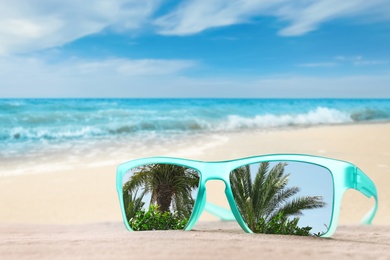 Image of Palms mirroring in sunglasses on sandy beach near ocean 