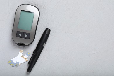 Glucometer, lancet pen and strips on grey table, flat lay with space for text. Diabetes testing kit