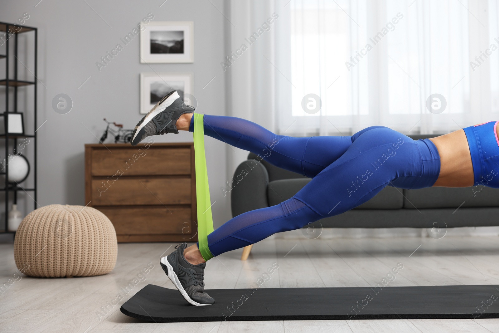 Photo of Woman doing exercise with fitness elastic band on mat at home, closeup