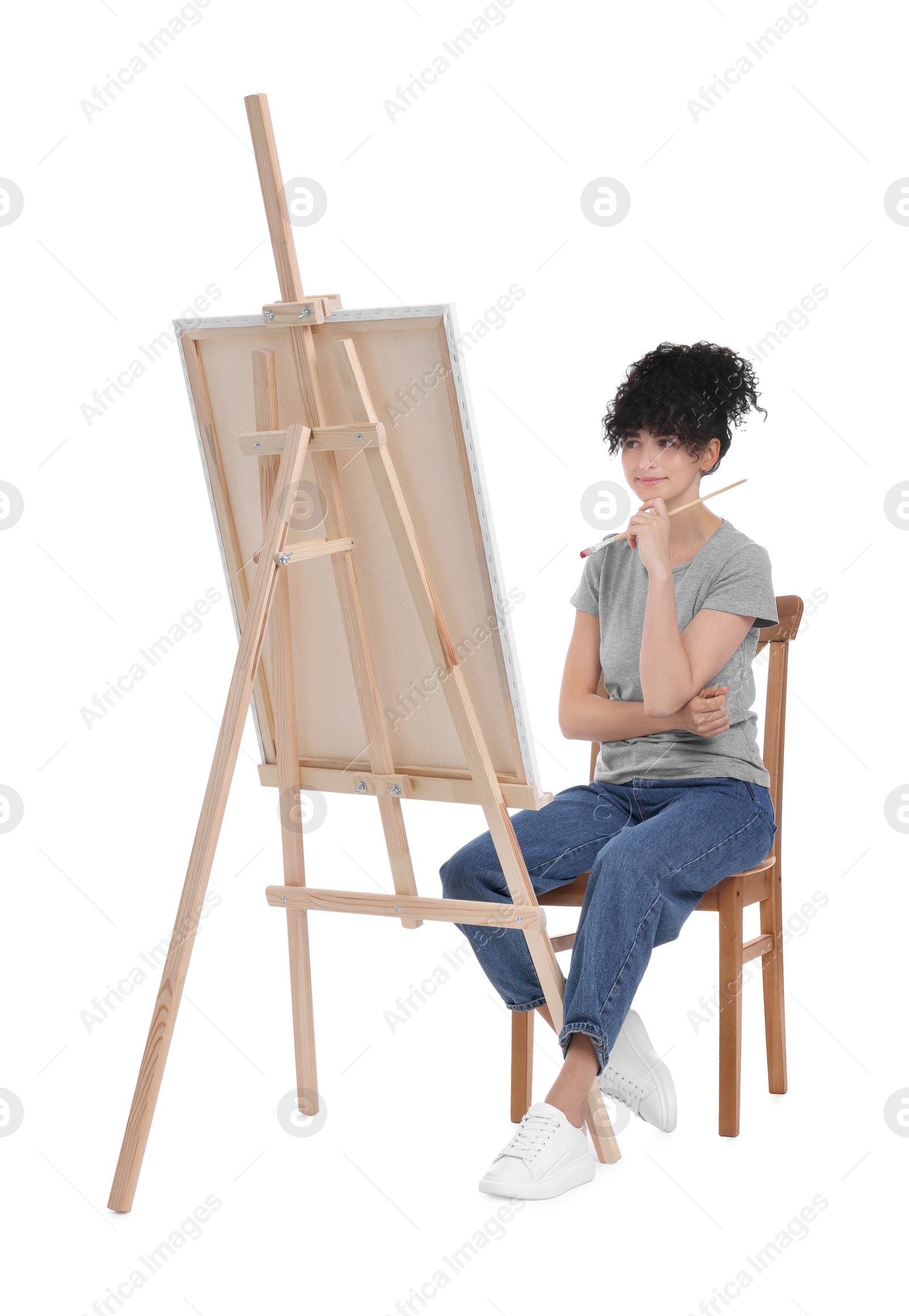 Photo of Young woman holding brush near easel with canvas against white background