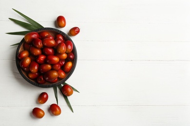 Palm oil fruits in bowl on white wooden table, flat lay. Space for text