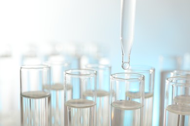 Dripping liquid from pipette into test tube on light background, closeup