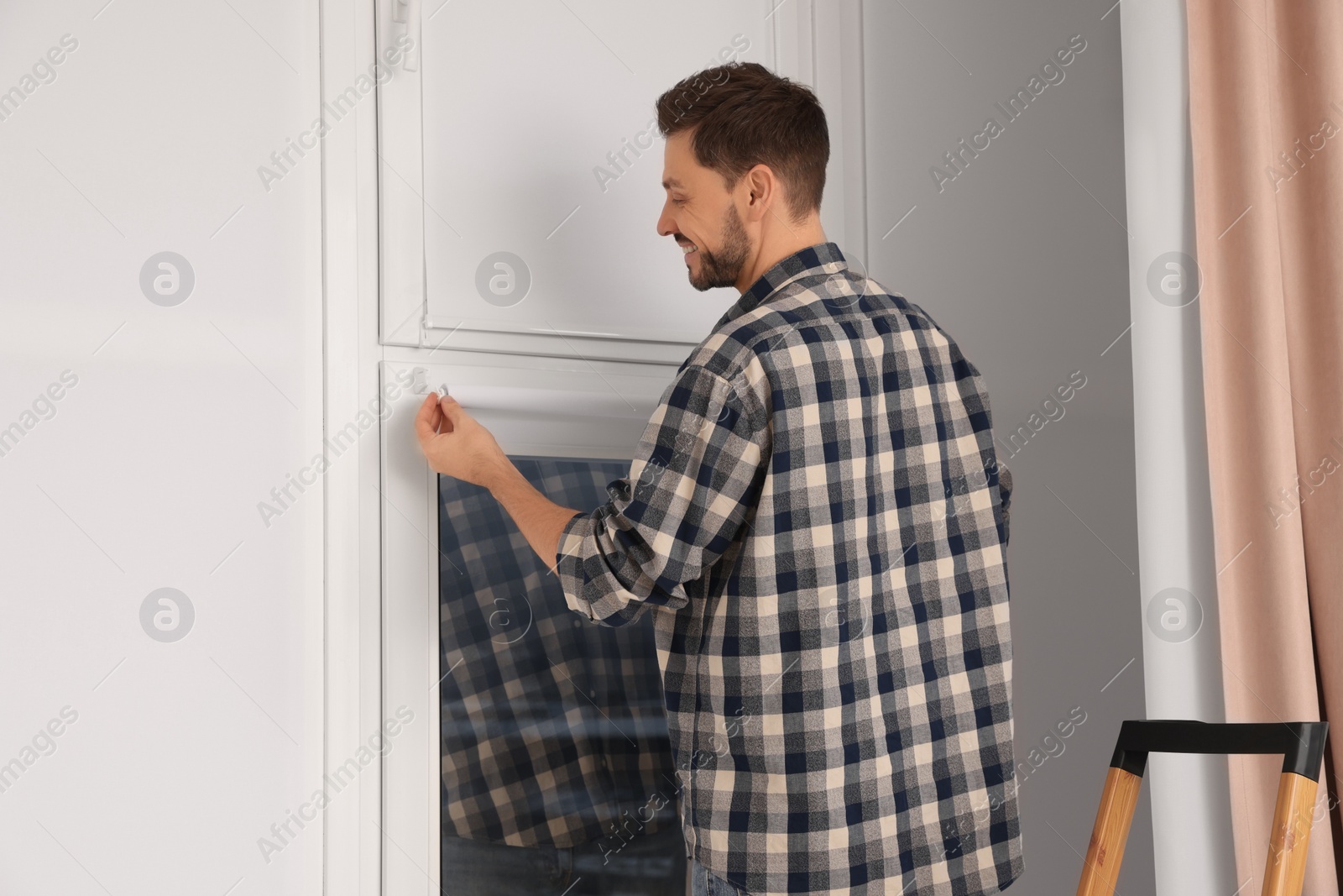 Photo of Man installing modern roller window blind indoors