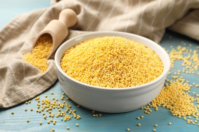 Millet groats in bowl on light blue wooden table, closeup