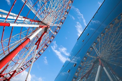 Photo of Beautiful large Ferris wheel near building against blue sky, low angle view