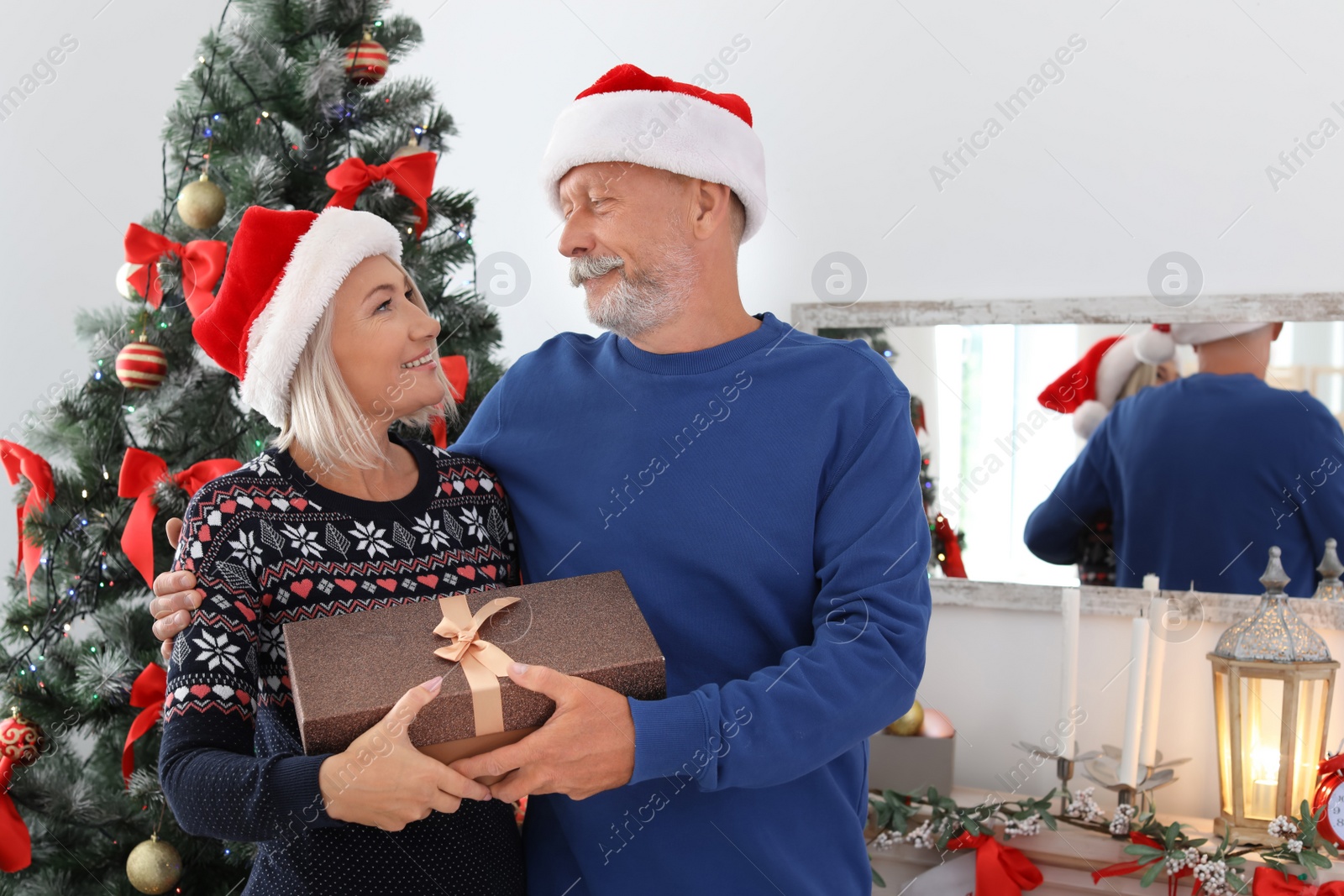 Photo of Mature couple in Santa hats with Christmas gift box at home