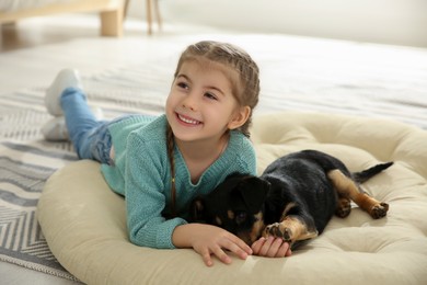 Photo of Little girl with cute puppy lying on soft pillow at home