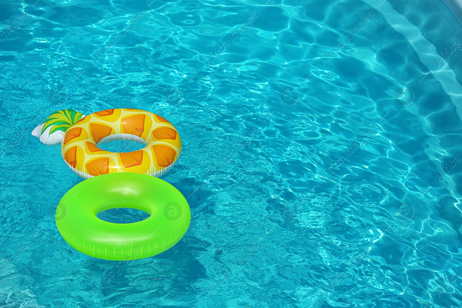 Photo of Bright inflatable rings floating in swimming pool on sunny day. Space for text