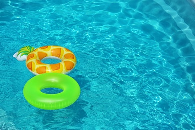 Photo of Bright inflatable rings floating in swimming pool on sunny day. Space for text