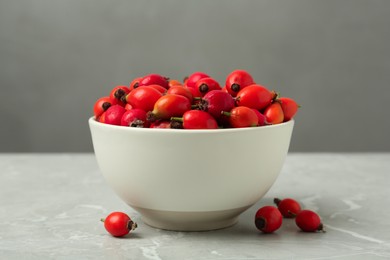 Photo of Ceramic bowl with rose hip berries on grey table, closeup. Cooking utensil