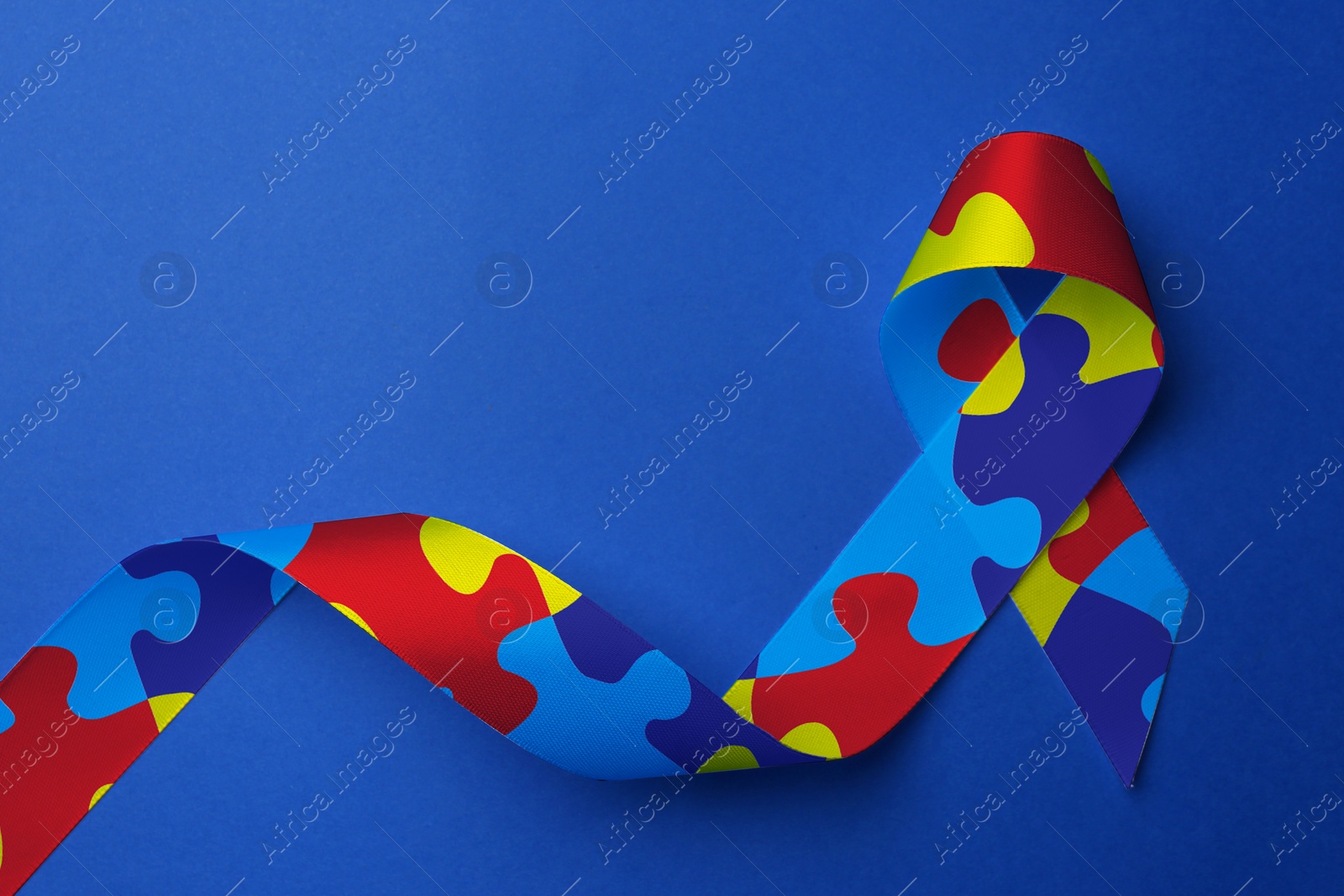 Image of World Autism Awareness Day. Colorful puzzle ribbon on blue background, top view