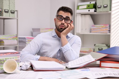 Overwhelmed man surrounded by documents at workplace in office