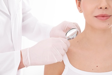 Dermatologist examining patient with magnifying glass in clinic, closeup view