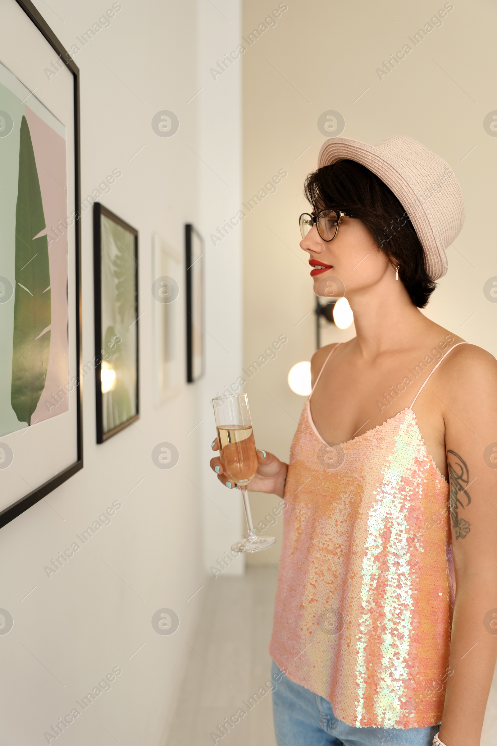 Photo of Young woman with glass of champagne at exhibition in art gallery