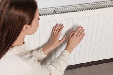 Photo of Woman warming hands on white heating radiator indoors, closeup