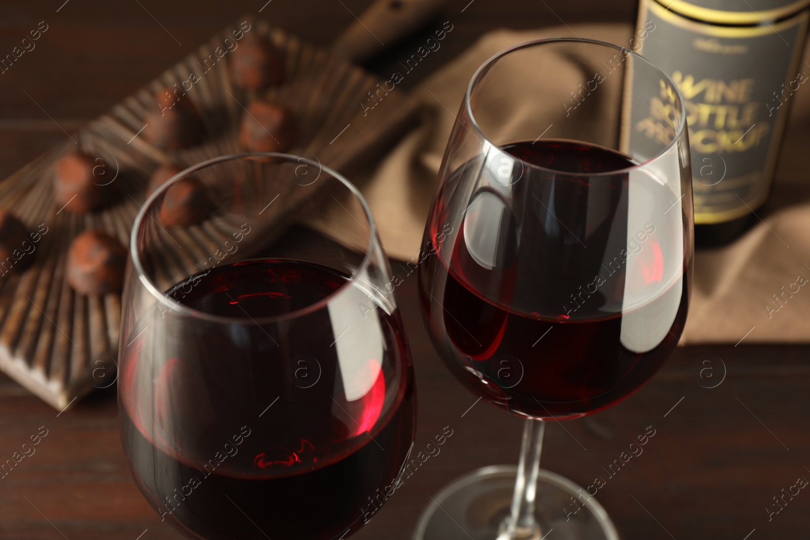 Photo of Glasses of red wine with chocolate candies on wooden table, closeup