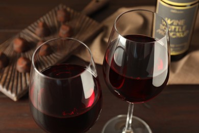 Photo of Glasses of red wine with chocolate candies on wooden table, closeup